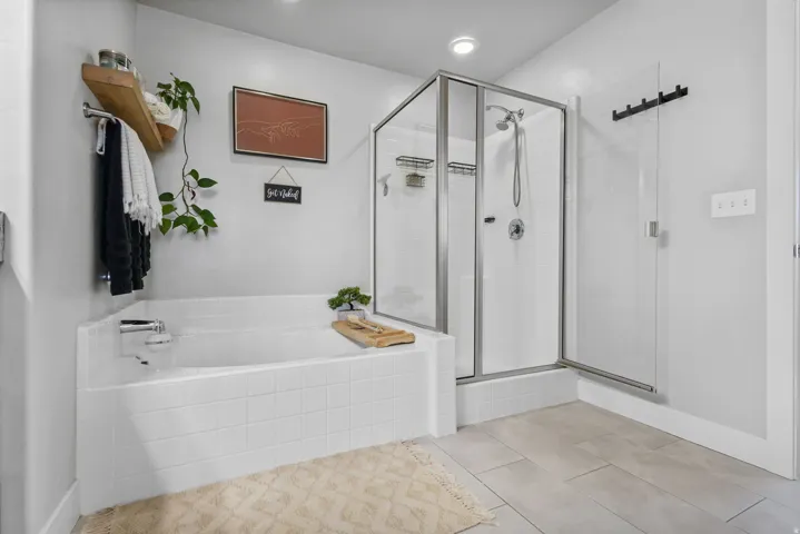 Tiled soaking tub and separate glass-enclosed shower featuring a handheld showerhead