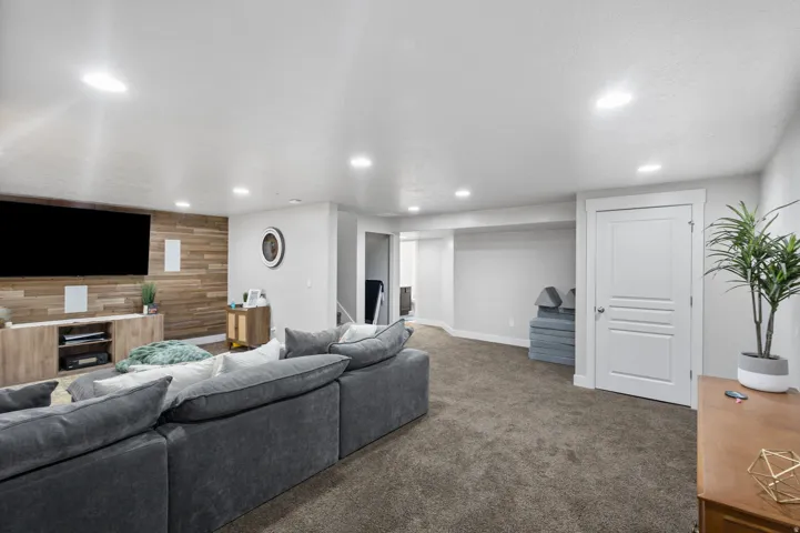 Spacious entertainment area featuring a wood-panel accent wall, recessed lighting, and neutral carpeting
