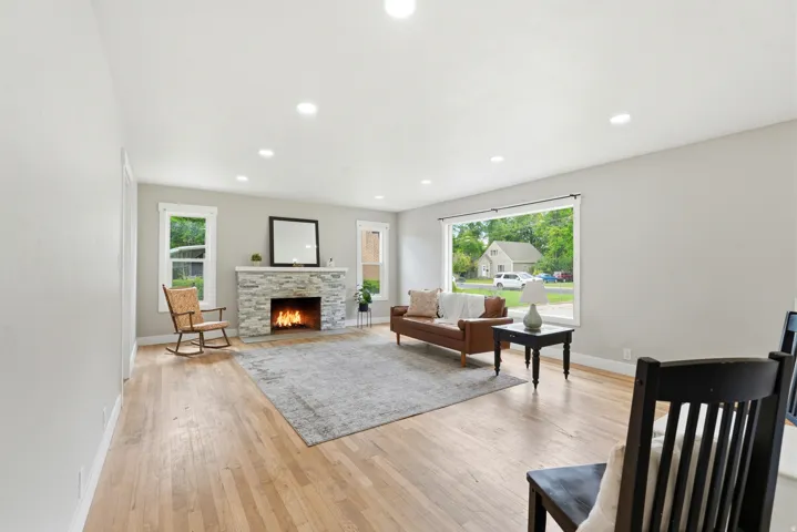 Spacious living area featuring light wood-finish flooring, a stone-clad fireplace, recessed lighting, large picture windows, and multiple additional windows