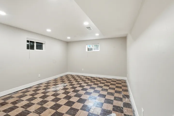 Spacious room featuring checkerboard flooring, light gray walls, recessed lighting, and two windows with white blinds