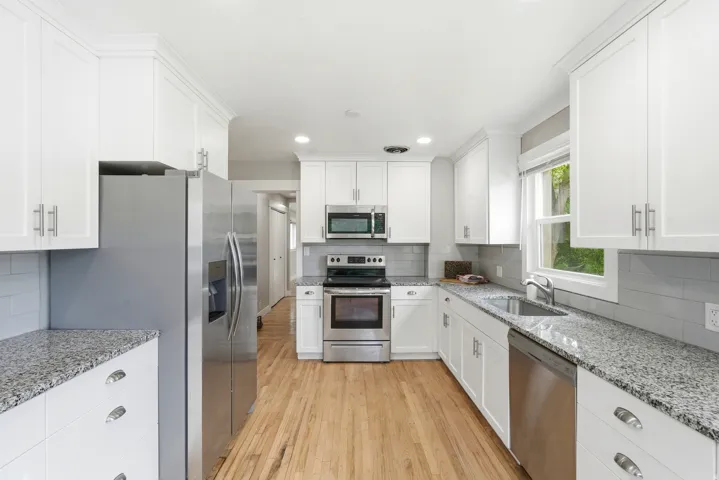 Kitchen featuring white cabinetry, speckled countertops, stainless steel appliances, wood-finish flooring, and a subway tile backsplash