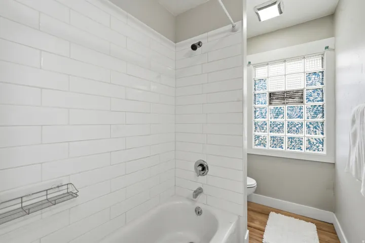 Bathroom featuring a white subway tile surround, chrome fixtures, and a glass block window with patterned accents