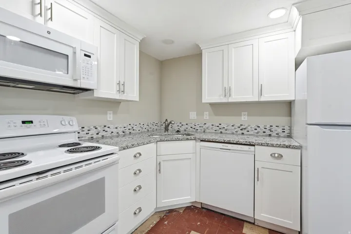 Kitchen featuring white cabinetry with brushed nickel hardware, light-toned countertops, a mosaic tile backsplash, and white appliances including a range, microwave, and dishwasher