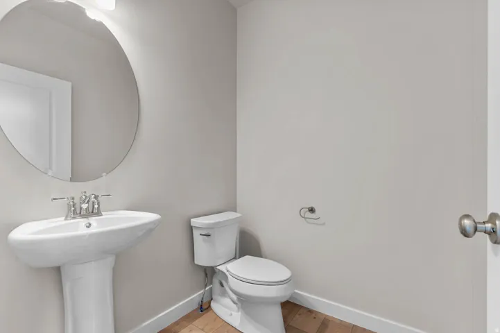 Pedestal sink with a chrome faucet, large circular wall mirror, and neutral wall tones