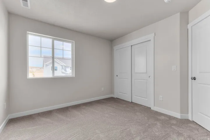 Spacious room with plush carpet flooring, a large window with white framing, and two white sliding closet doors