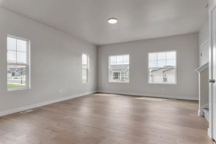 Spacious room featuring wood-finish flooring, light-toned walls, multiple windows with grid patterns, and white trim throughout