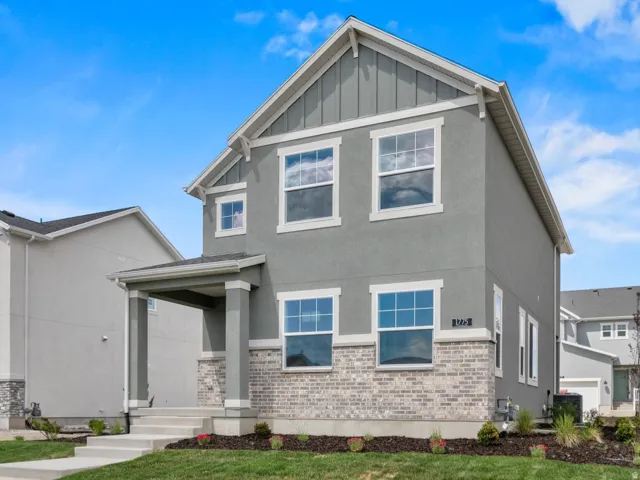 Two-story residence featuring a covered entry, board and batten siding details, stucco exterior, stone veneer accents, and a concrete pathway