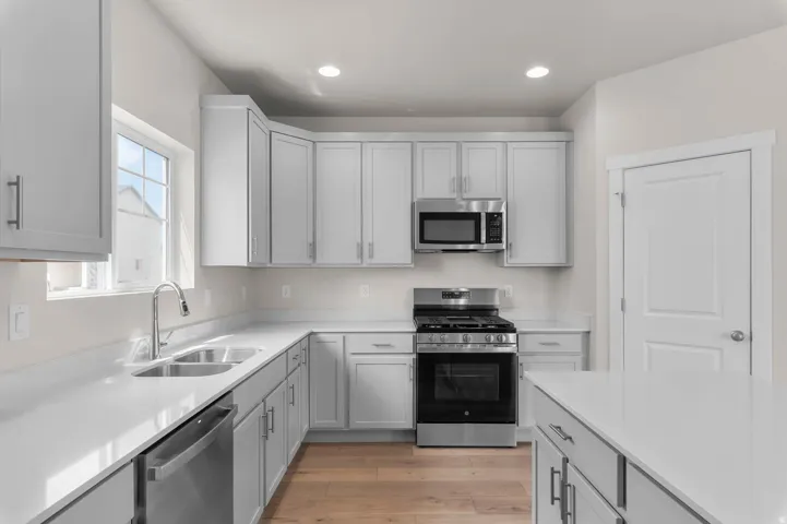Modern kitchen featuring light gray cabinetry, stainless steel appliances, white countertops, and wood-finish flooring