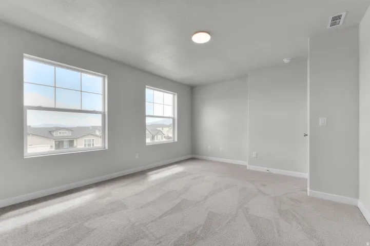 Spacious room featuring two large windows with grid patterns, light gray walls, plush gray patterned carpeting, and white baseboards