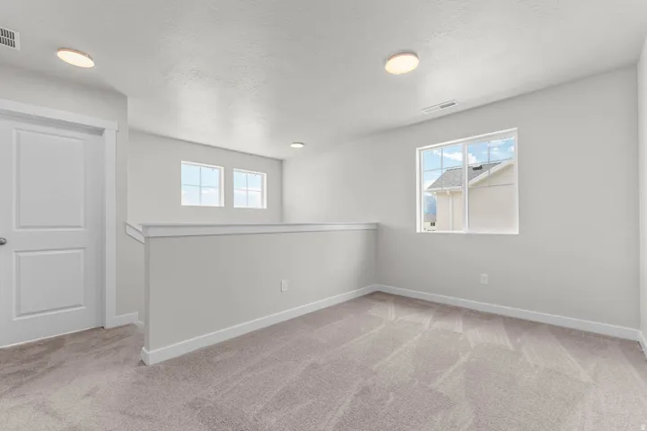 Carpeted loft space featuring multiple windows, a white paneled door, and recessed lighting fixtures