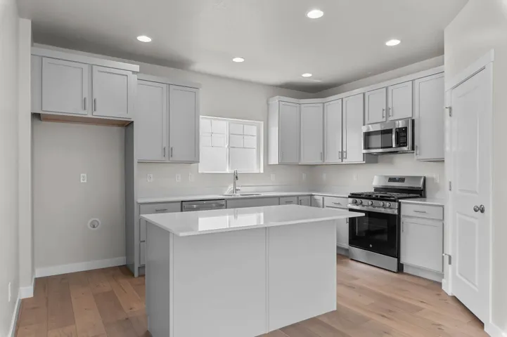 Bright kitchen featuring an island with a light-toned countertop, wood-finish flooring, recessed lighting, sleek cabinetry, and stainless steel appliances