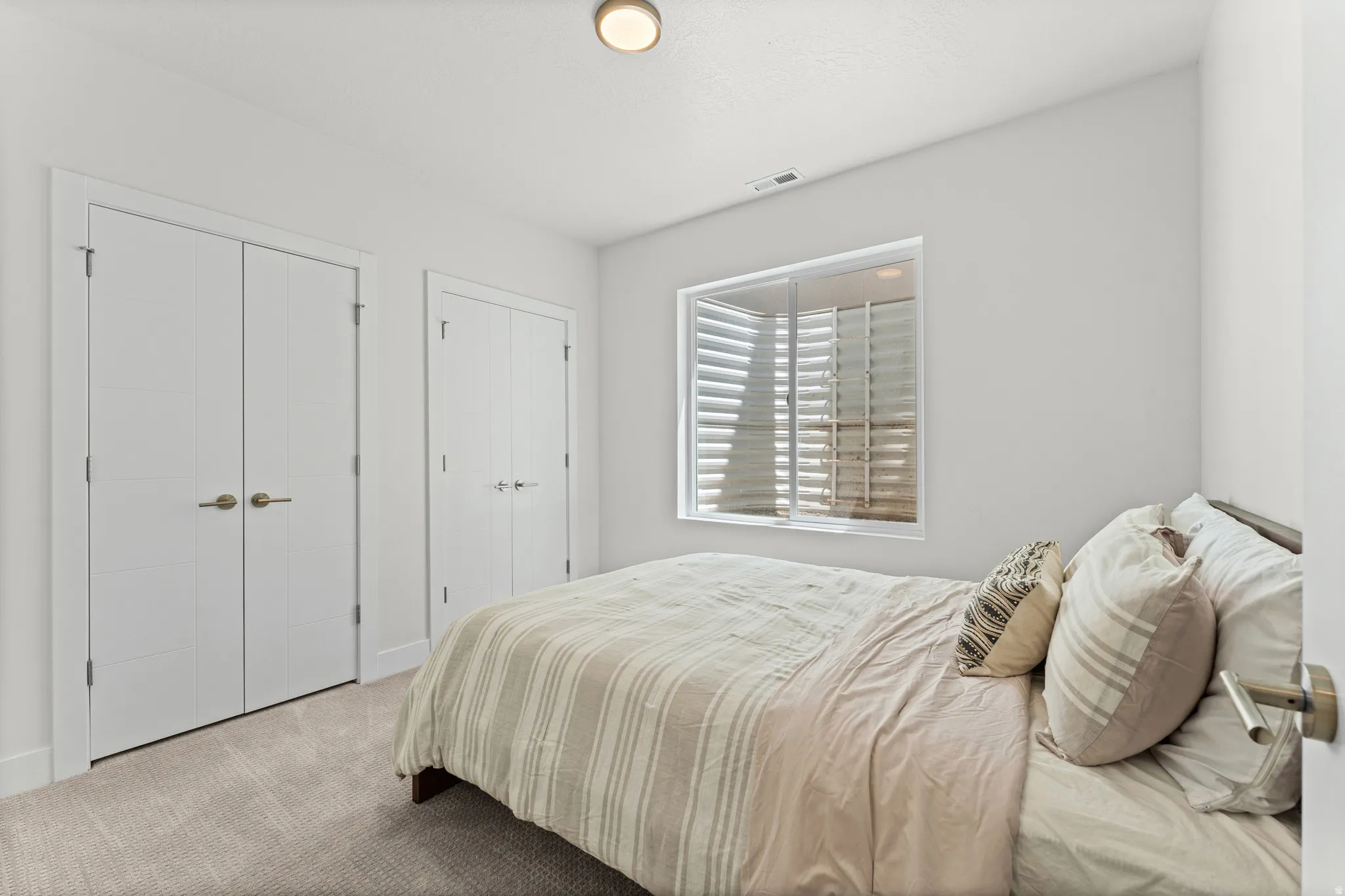 Room featuring neutral wall tones, carpet flooring, a window with plantation shutters, a flush-mount ceiling light, and two bifold closet doors