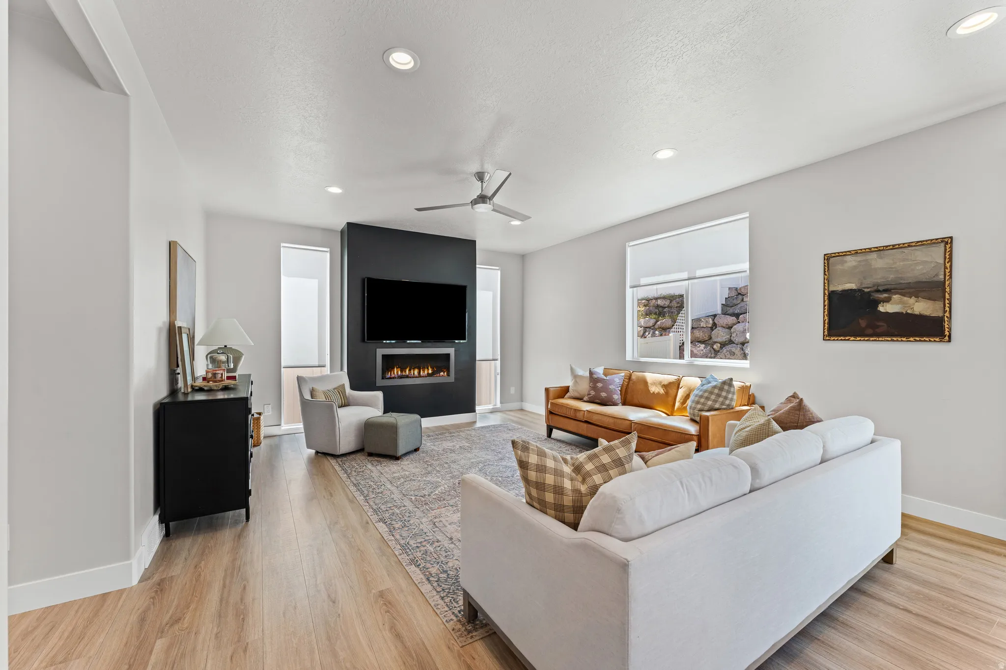 Open-concept living space with wood-finish flooring, a contemporary fireplace feature wall, recessed lighting, and a ceiling fan