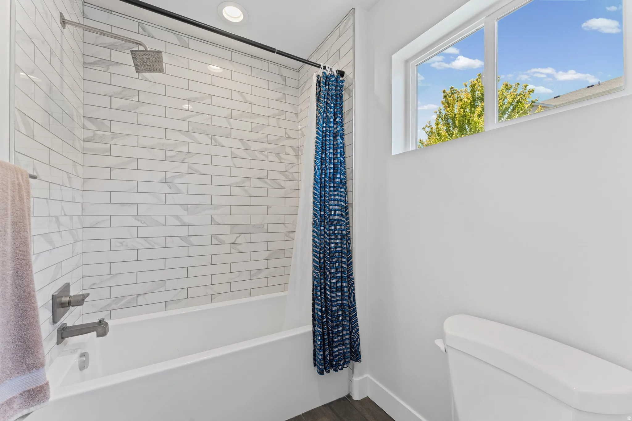 Bathroom featuring white subway tile shower surround with geometric accents, brushed nickel fixtures, a white soaking tub, and a window providing natural light