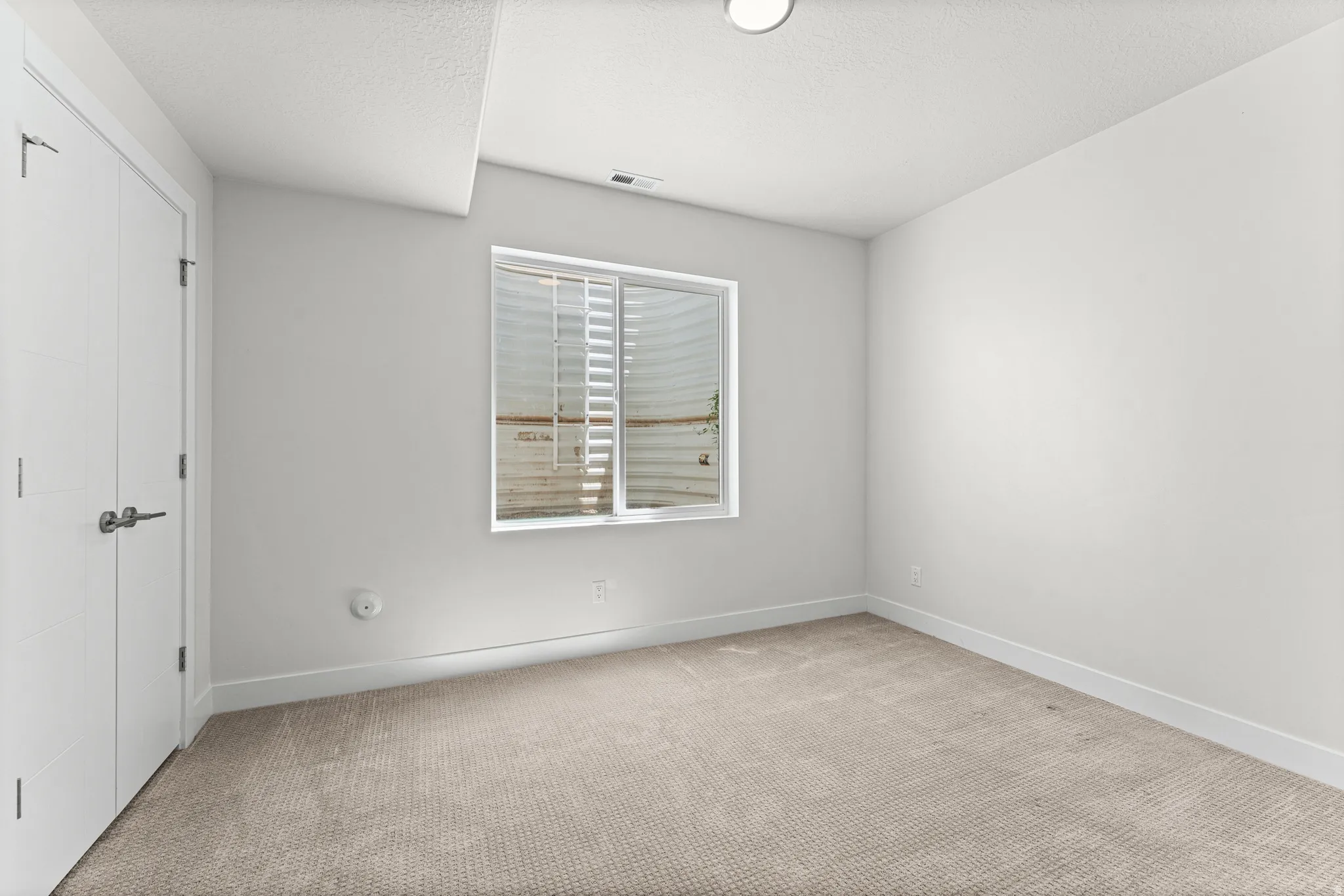 Carpeted interior space featuring white walls and a large window with blinds