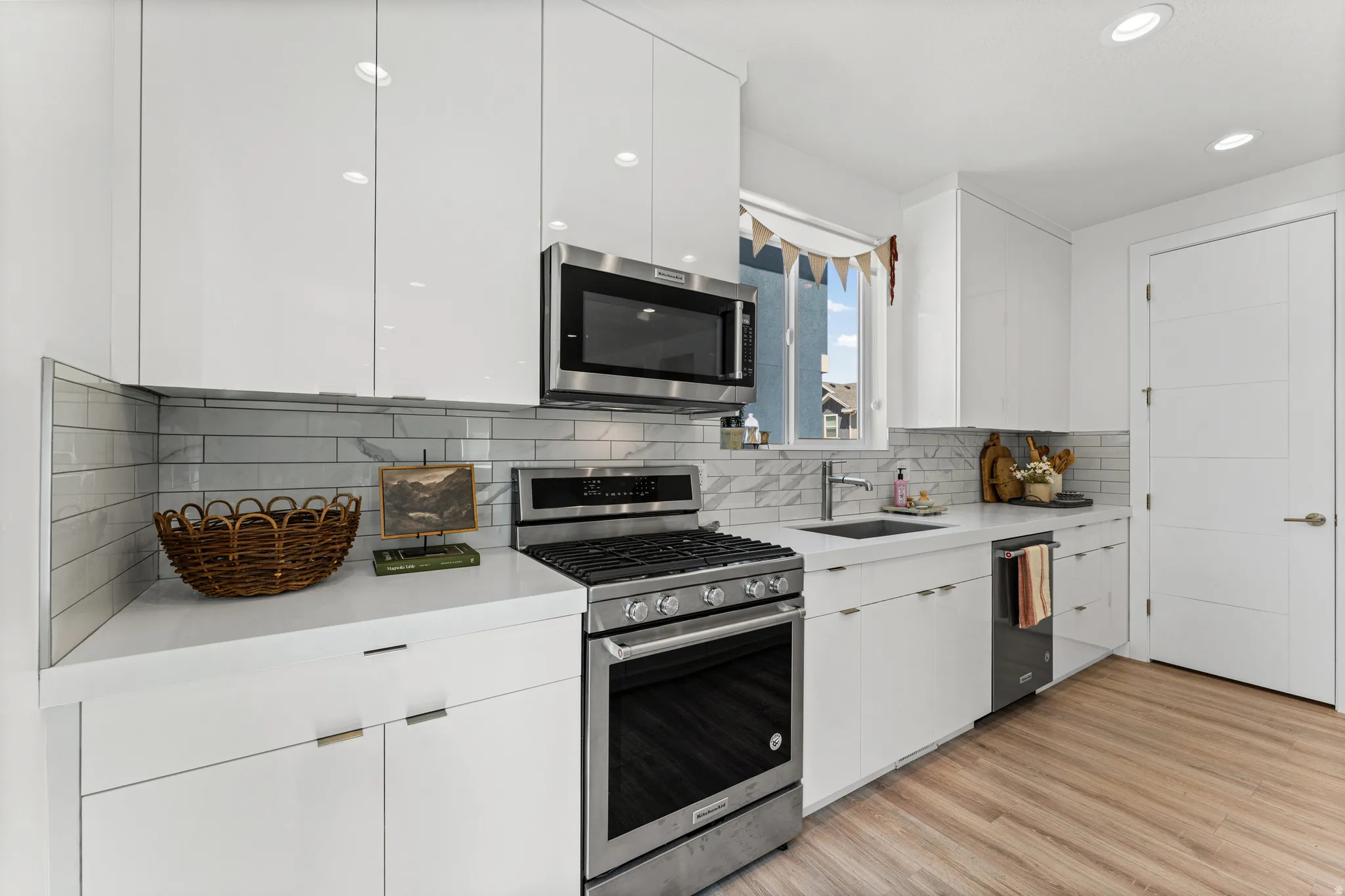 Modern kitchen featuring white flat-panel cabinetry, stainless steel appliances, a subway tile backsplash, light-toned countertops, and wood-finish flooring