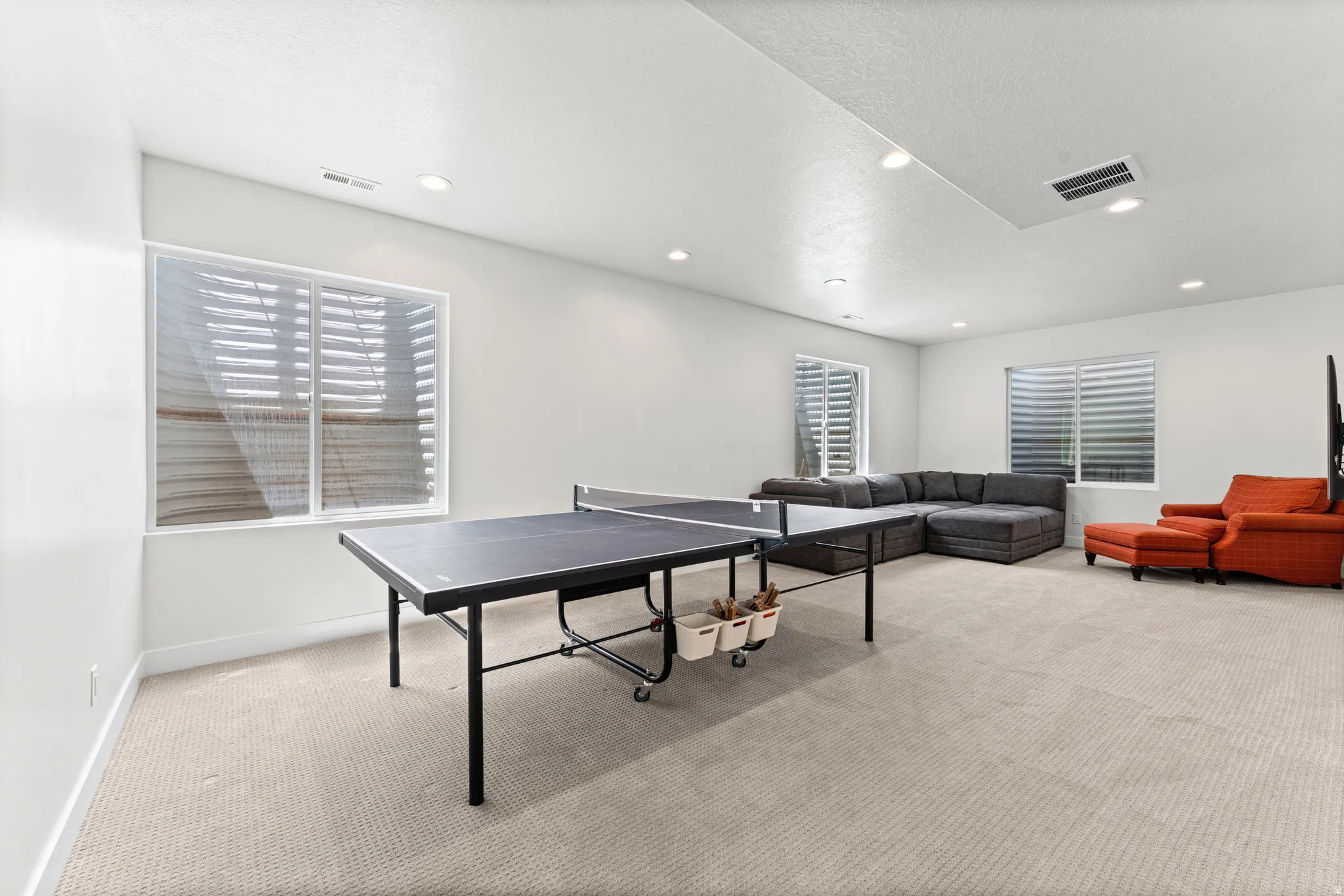 Spacious recreation room featuring light-toned carpeting and multiple windows with horizontal blinds