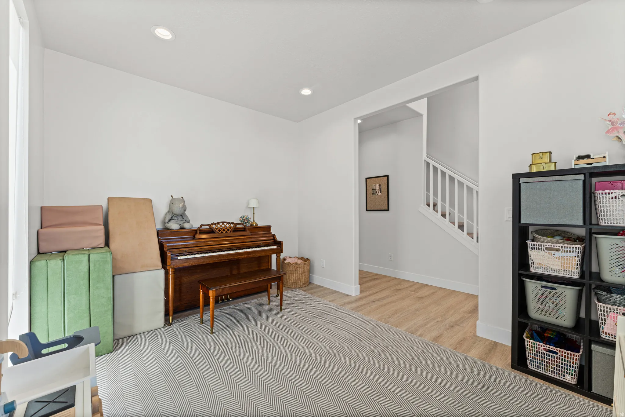 Versatile room featuring light-toned walls, recessed lighting, and a combination of wood-finish flooring and patterned carpeting