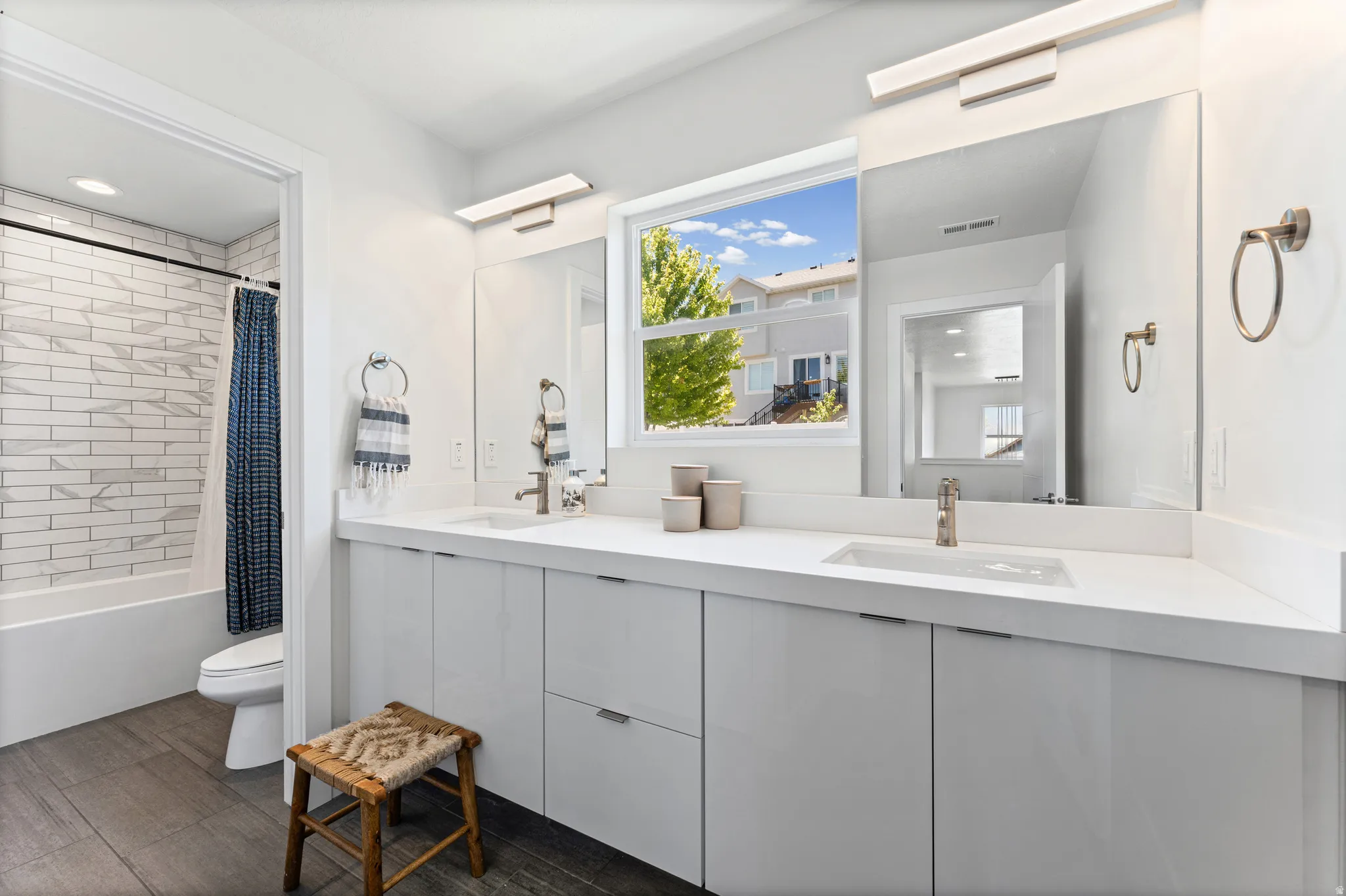 Bathroom featuring a dual vanity with white cabinetry and integrated sinks, under-mirror lighting, and wood-finish flooring