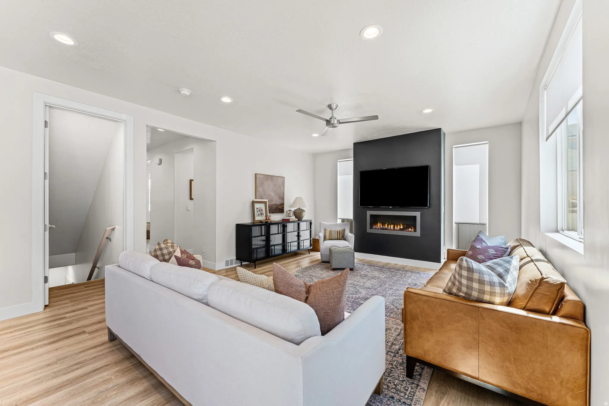 Open-concept living space featuring wood-finish flooring, recessed lighting, and a linear electric fireplace integrated into a contrasting accent wall