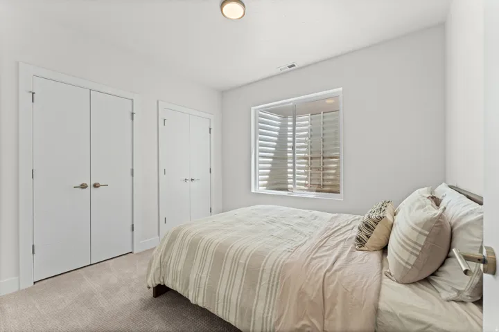 Room featuring neutral wall tones, carpet flooring, a window with plantation shutters, a flush-mount ceiling light, and two bifold closet doors