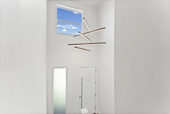 Two-story entry featuring high ceilings, a contemporary linear chandelier, a transom window, and a white entry door with a horizontal pull handle