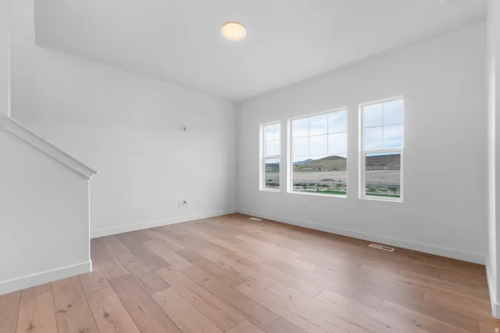 Spacious interior room featuring light wood-finish flooring, white baseboards, and a neutral wall color