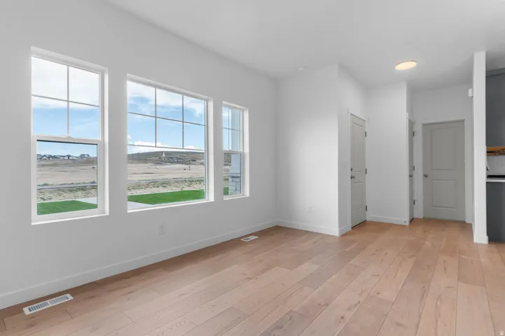 Bright interior space featuring three large windows with grid muntins, light wood-finish flooring, white baseboards, and ceiling-mounted lighting