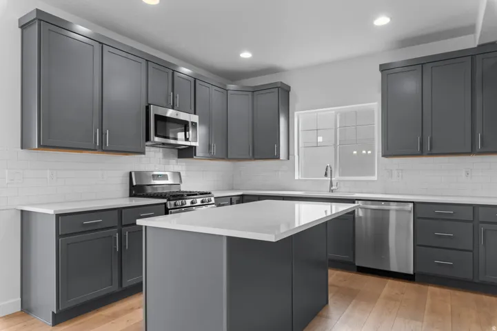 Modern kitchen featuring gray cabinetry, white countertops, stainless steel appliances, a center island, and wood-finish flooring