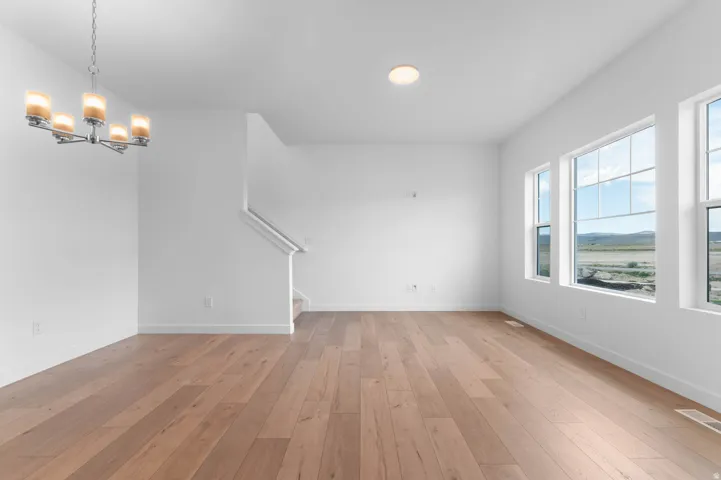 Spacious interior featuring wood-finish flooring, a contemporary chandelier, multiple windows with grid detailing, a flush-mount ceiling light, and a visible staircase