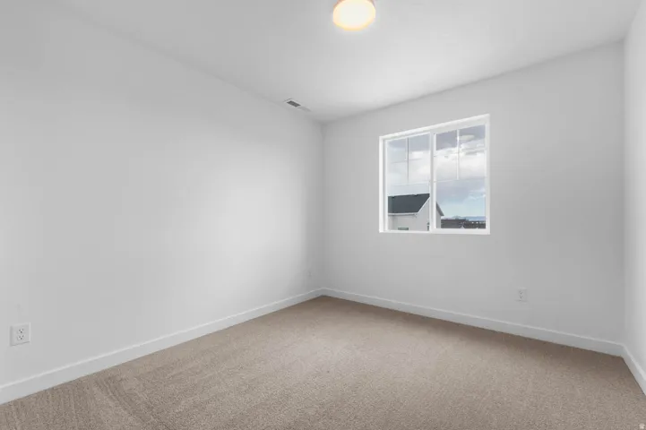 Bright interior space featuring light-colored carpeting, white baseboards, and a single window with white framing