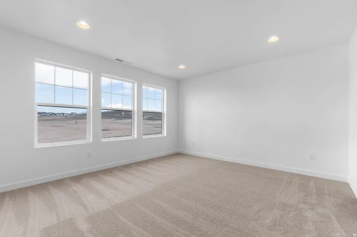 Light-filled interior featuring three large windows, recessed ceiling lighting, textured carpeting, and bright white walls