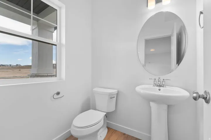 Bright interior space featuring a pedestal sink, oval mirror, and a window with exterior views