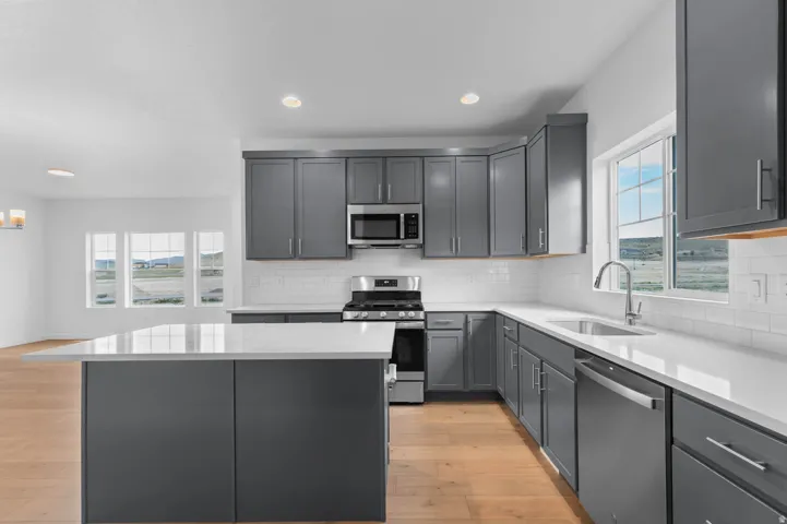 Kitchen featuring gray cabinetry, stainless steel appliances, a white subway tile backsplash, and light wood-finish flooring