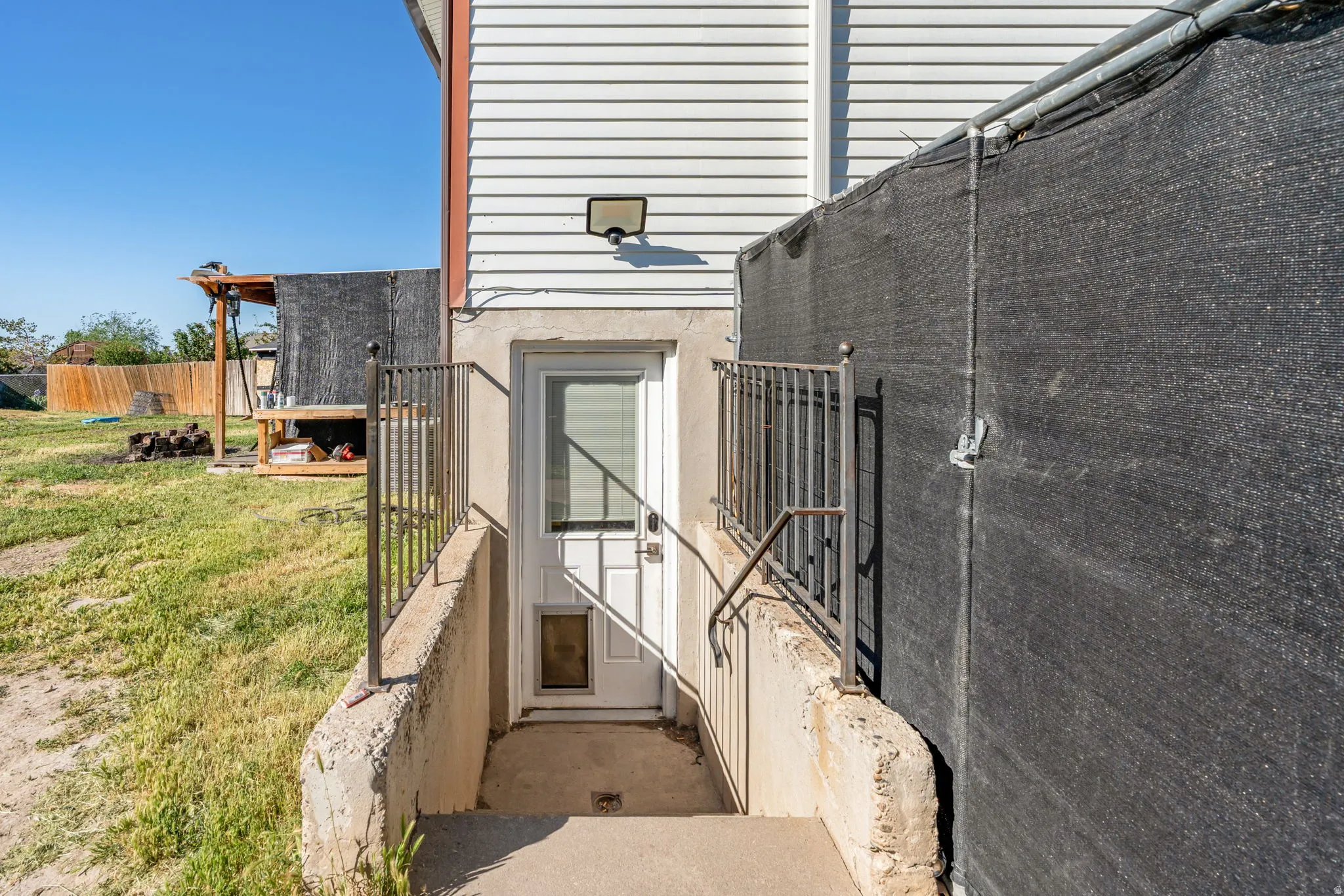 Exterior basement entry with a white door, concrete steps, and metal handrails