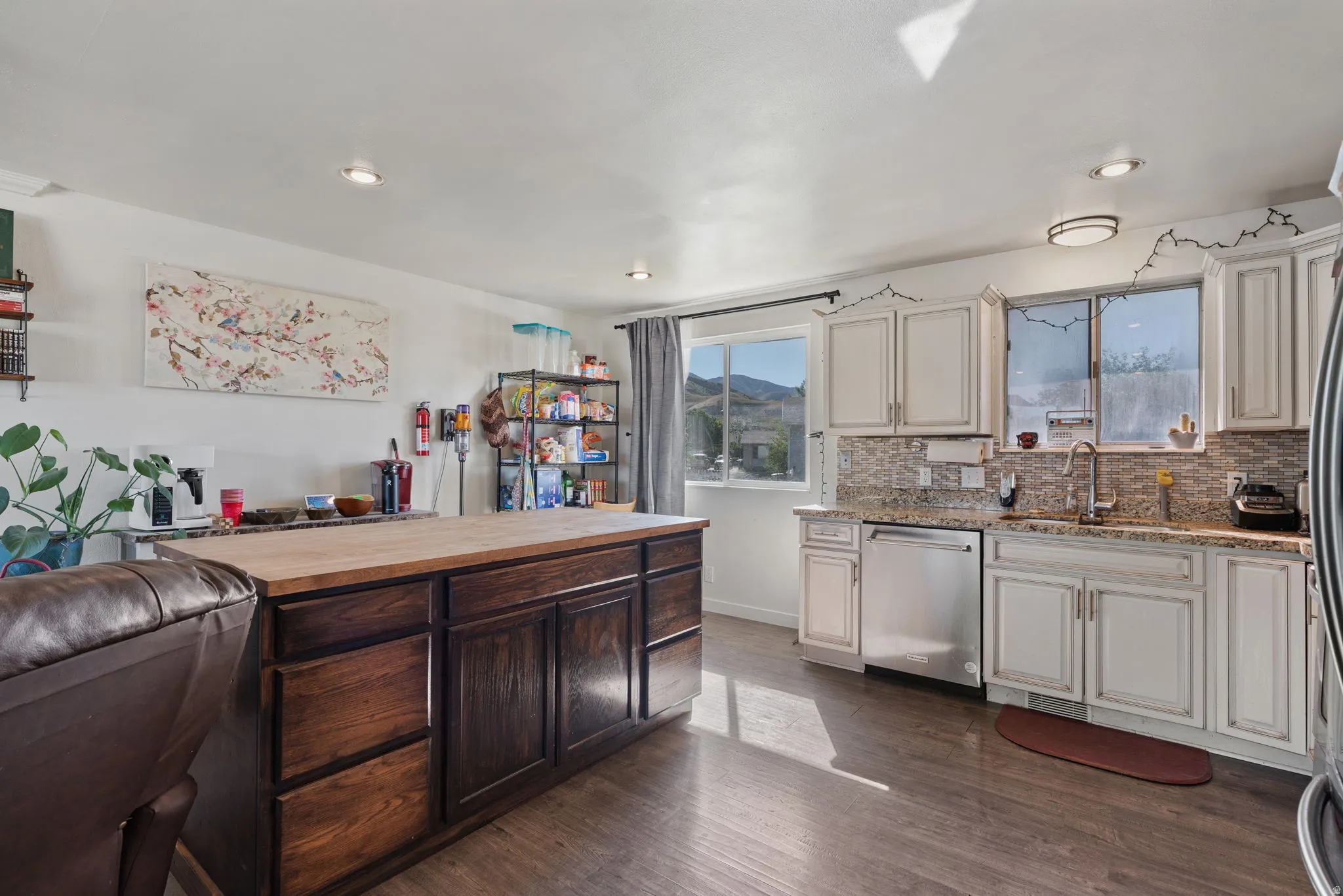 Open-concept kitchen with wood-finish flooring, white cabinetry, stainless steel appliances, and a mosaic tile backsplash