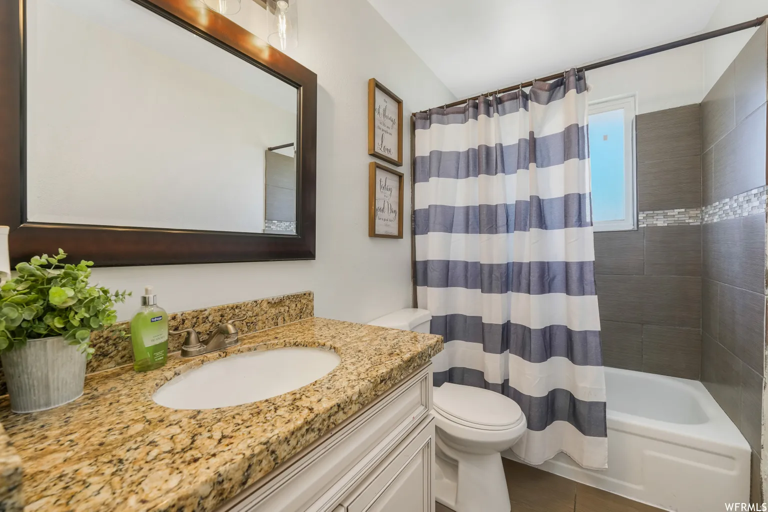Bathroom featuring a granite-look countertop with an undermount sink, a framed mirror, and a full bathtub with a tiled surround