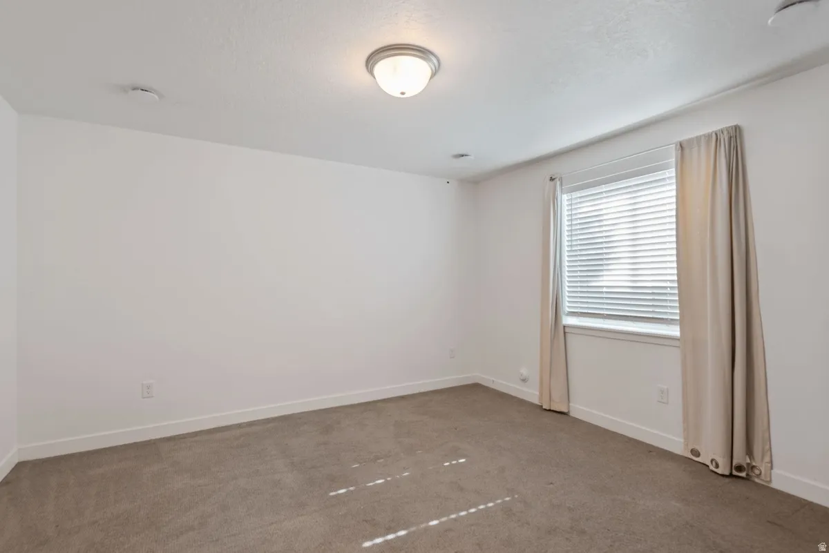 Carpeted room featuring a single window with blinds and drapes, a flush-mount ceiling light fixture, and white baseboards