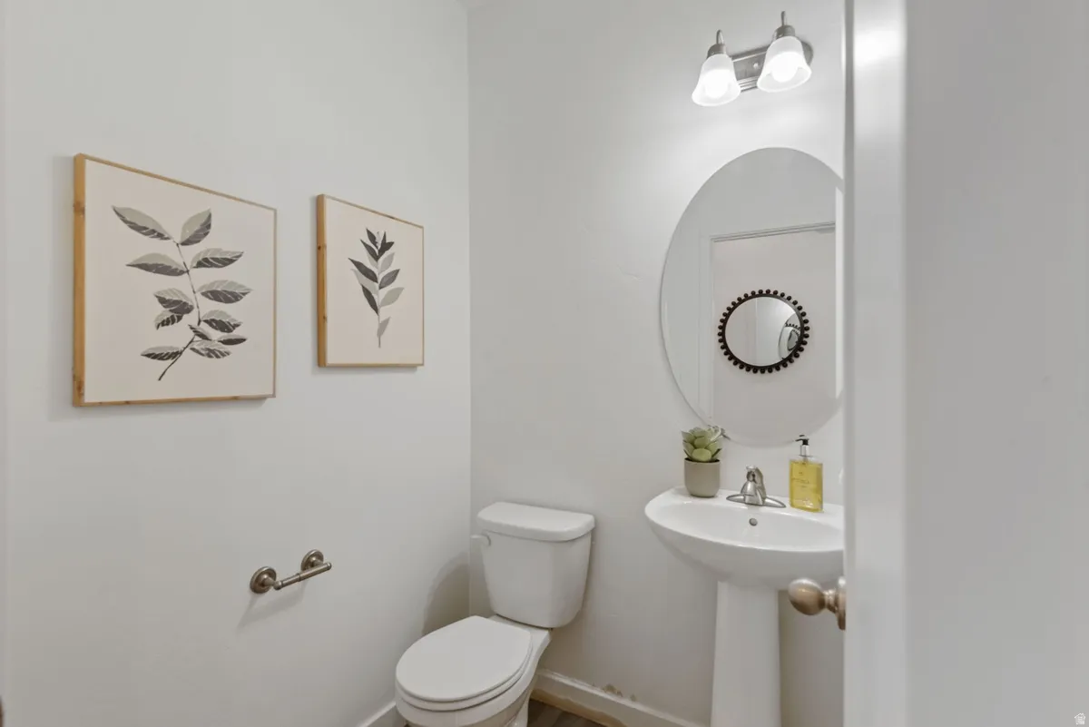 Bathroom featuring a pedestal sink with a single-handle faucet, oval mirror, and a two-bulb vanity light fixture