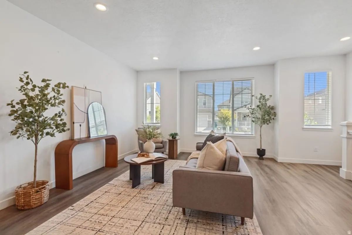 Spacious living area featuring light wood-finish flooring, recessed lighting, and ample natural light from multiple windows