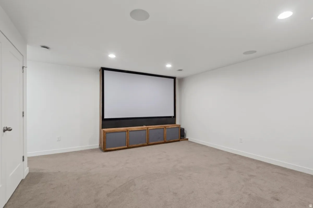 Dedicated media room featuring a large projection screen, built-in media console, recessed lighting, integrated ceiling speakers, and neutral carpet flooring