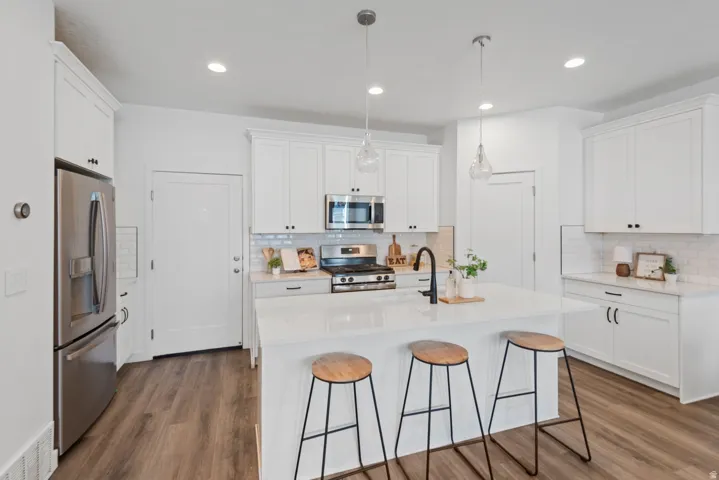 Modern kitchen featuring a central island, white shaker cabinetry, stainless steel appliances, wood-finish flooring, and subway tile backsplash