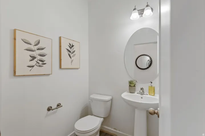 Bathroom featuring a pedestal sink with a single-handle faucet, oval mirror, and a two-bulb vanity light fixture