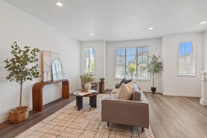 Spacious living area featuring light wood-finish flooring, recessed lighting, and ample natural light from multiple windows