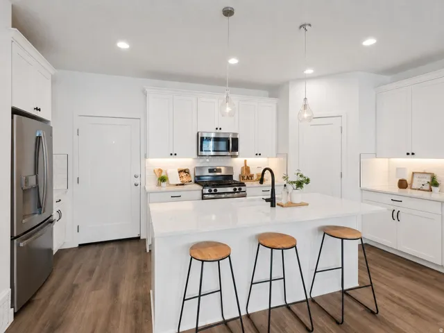 Kitchen featuring a central island with a matte black faucet, white shaker-style cabinetry, stainless steel appliances, wood-finish flooring, and pendant lighting
