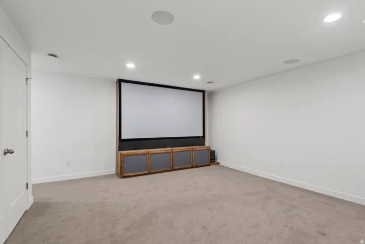 Dedicated media room featuring a large projection screen, built-in media console, recessed lighting, integrated ceiling speakers, and neutral carpet flooring