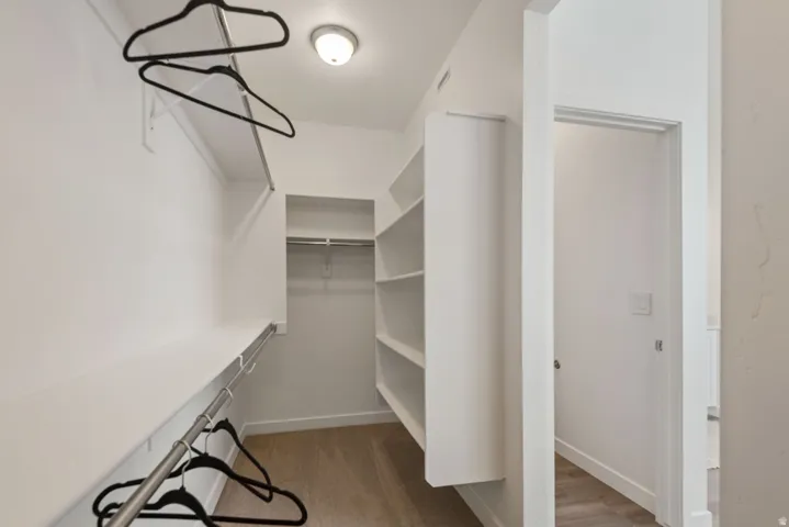 Walk-in closet featuring built-in shelving, multiple hanging rods, and wood-finish flooring
