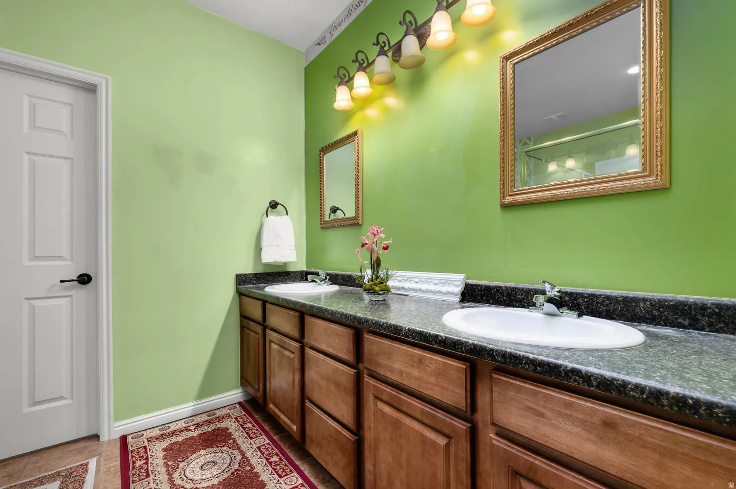 Dual vanity with a speckled countertop, brown wood cabinetry, and twin framed mirrors