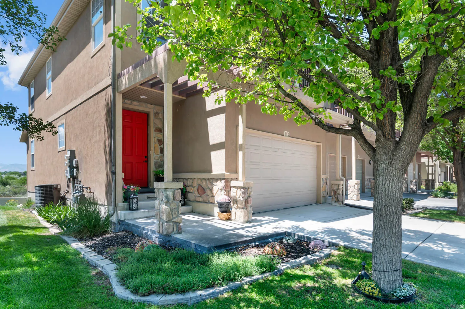 Stucco exterior with stone accents, featuring a bright red entry door, a covered porch, and an attached garage