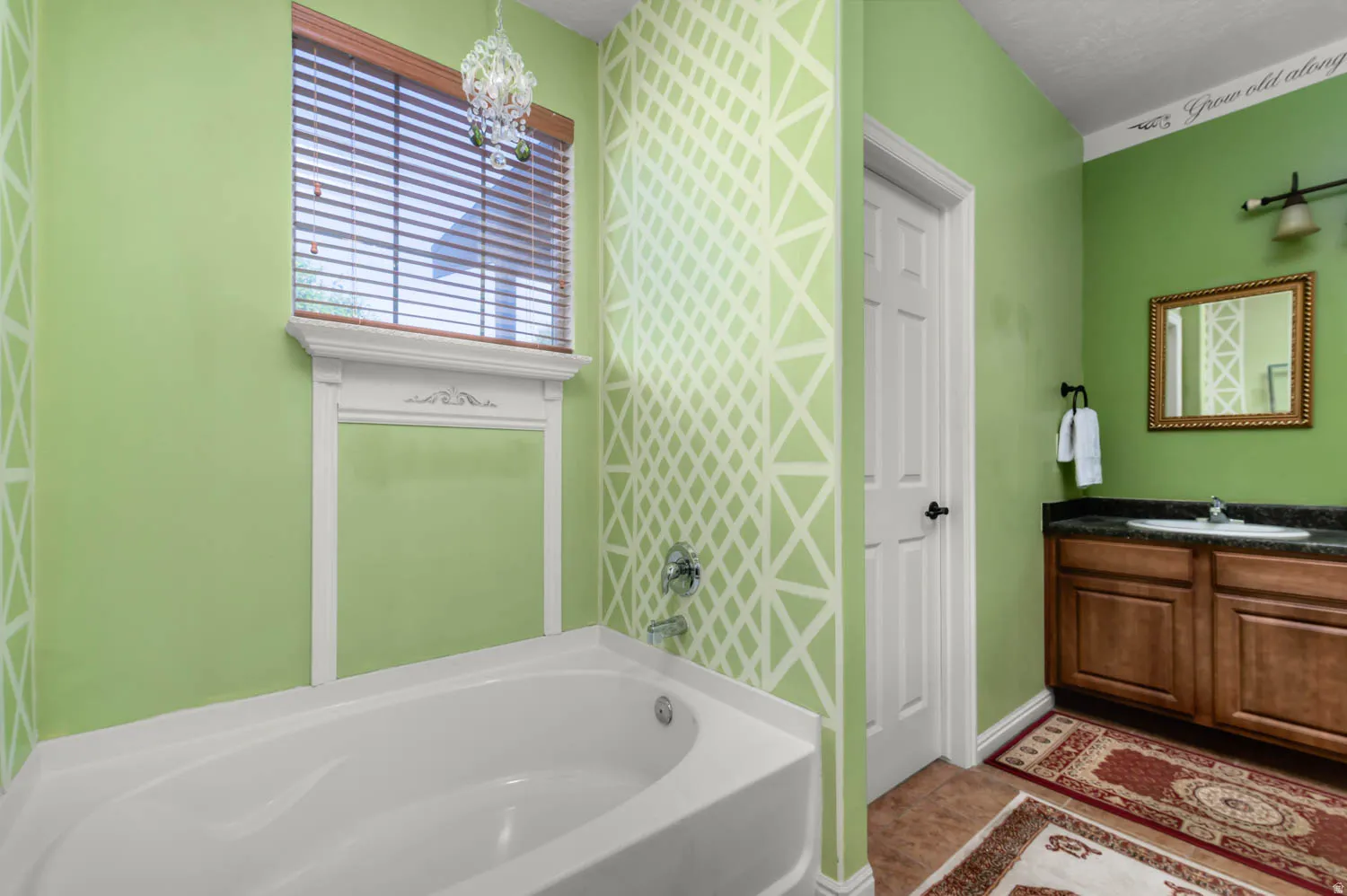 White soaking tub with decorative window surround, light green walls, and decorative geometric wall pattern